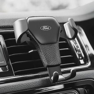 May include: Black car phone holder with the Ford logo. The holder is designed to attach to a car's air vent. The holder is made of black plastic and has a textured grip area. The holder has a curved design to securely hold a phone.