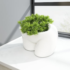 May include: White ceramic planter shaped like a human figure, with a green plant growing inside.