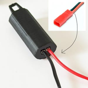 May include: A black, rectangular, 3D-printed plastic housing with a mounting loop at one end. Two electrical wires, one black and one red, extend from the housing. An inset image shows a red T-style electrical connector attached to the wires.