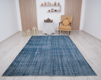 May include: A blue distressed area rug with a subtle pattern. The rug is laid out on a light wood floor in a room with white walls.