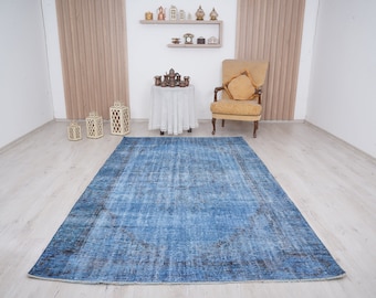 May include: A blue vintage rug with a faded pattern, placed on a light wood floor in a room with white walls and a yellow armchair.