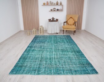 May include: A teal blue vintage rug with a distressed look. The rug is laid out on a light wood floor in a room with white walls.