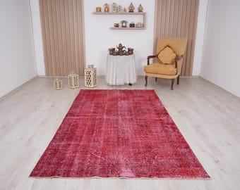 Könnte beinhalten: Ein Vintage-Teppich in Rot und Rosa mit einem abgenutzten Look. Der Teppich liegt auf einem hellen Holzboden in einem Raum mit einem Stuhl und Dekoartikeln.