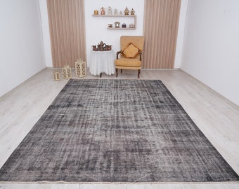 May include: A gray and white vintage distressed rug with a subtle geometric pattern. The rug is laid out on a light wood floor in a room with white walls and a chair.