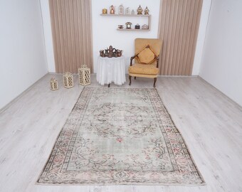 May include: A vintage-style rug with a faded floral pattern in shades of pink, green, and brown. The rug has a distressed look and is laid out on a light wood floor.