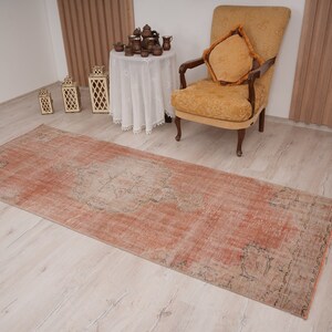 May include: A vintage runner rug in a faded peach color with a subtle pattern. The rug is laid out on a light wood floor.