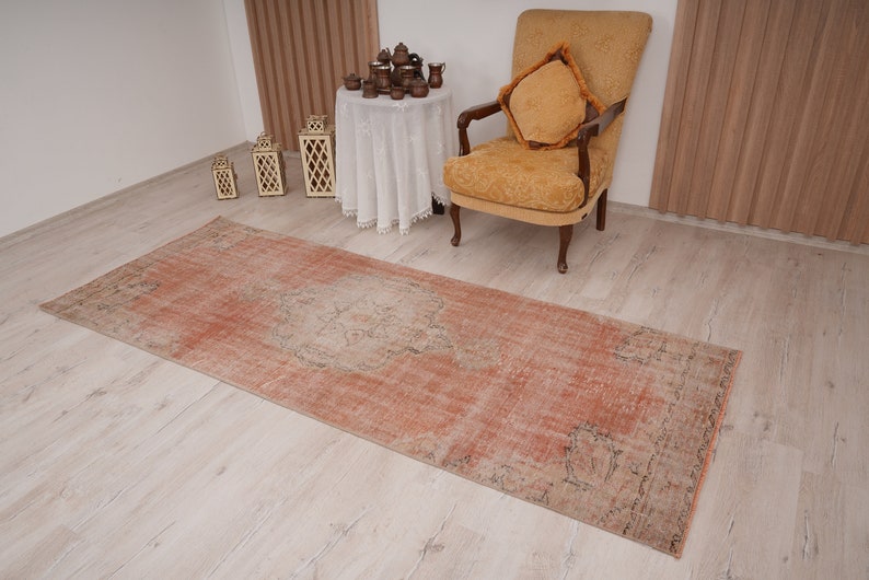 May include: A vintage runner rug in a faded peach color with a subtle pattern. The rug is laid out on a light wood floor.