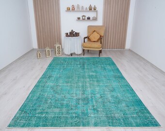 May include: A teal blue vintage rug with a faded pattern. The rug is laid out on a light wood floor in a room with white walls.