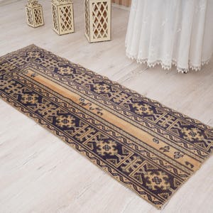 May include: A rectangular, vintage-style rug with a central beige stripe and navy blue geometric patterns. The rug is long and narrow, suitable for a hallway or entryway. The rug's dimensions are approximately 3 feet by 8 feet.
