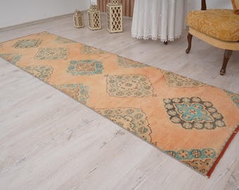 Op de afbeelding: Een lange, rechthoekige loper met een oranje achtergrond en herhalende geometrische patronen in teal, grijs en beige. De loper heeft een distressed, vintage look en ligt op een lichte houten vloer.