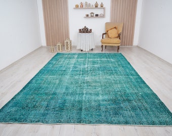 May include: A teal blue vintage rug with a distressed look. The rug is laid out on a light wood floor in a room with white walls.