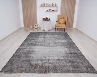 May include: A gray and white distressed area rug with a subtle pattern. The rug is laid out on a light wood floor in a room with white walls and a chair.
