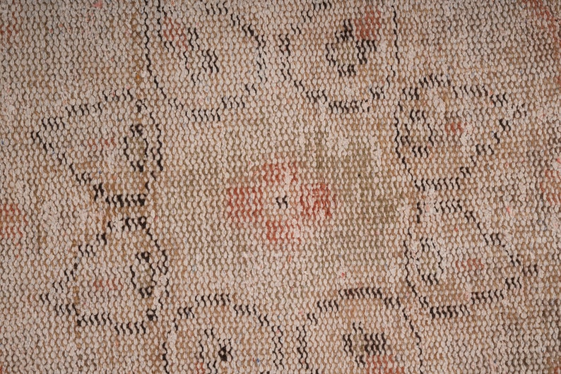 May include: Close-up of a beige woven rug with a repeating pattern of black and brown lines. The rug has a faded, vintage look with hints of red and orange.