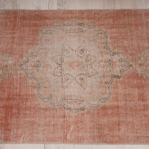 May include: A vintage runner rug with a faded, distressed look. The rug has a light orange background with a central medallion in a lighter shade. The medallion features a geometric design with a floral motif.