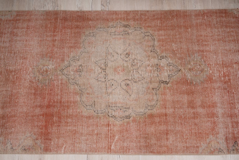 May include: A vintage runner rug with a faded, distressed look. The rug has a light orange background with a central medallion in a lighter shade. The medallion features a geometric design with a floral motif.