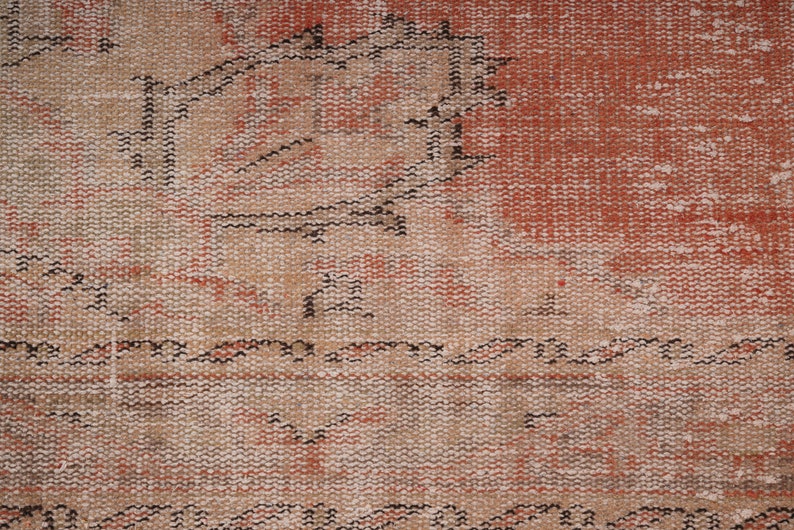 May include: Close-up of a woven rug with a faded red and beige pattern. The rug has a distressed look with a worn texture.