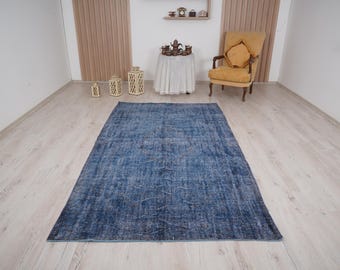 May include: A large, rectangular, distressed blue rug with a faded appearance. The rug is placed on a light-colored wooden floor, and the room features a chair, table, and decorative items.