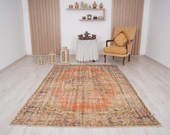 Può includere: Un tappeto in stile vintage con una combinazione di colori arancio, beige e marrone. Il tappeto ha un aspetto sbiadito e usurato e presenta un motivo floreale. Il tappeto è steso su un pavimento in legno chiaro in una stanza con pareti bianche.