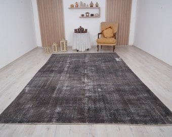 May include: A distressed gray and white vintage rug with a faded pattern. The rug is laid out on a light wood floor in a room with white walls and a chair.