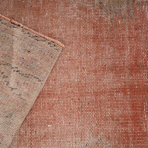 May include: Close-up of a woven rug with a faded red and white pattern. The rug has a textured surface and a frayed edge.