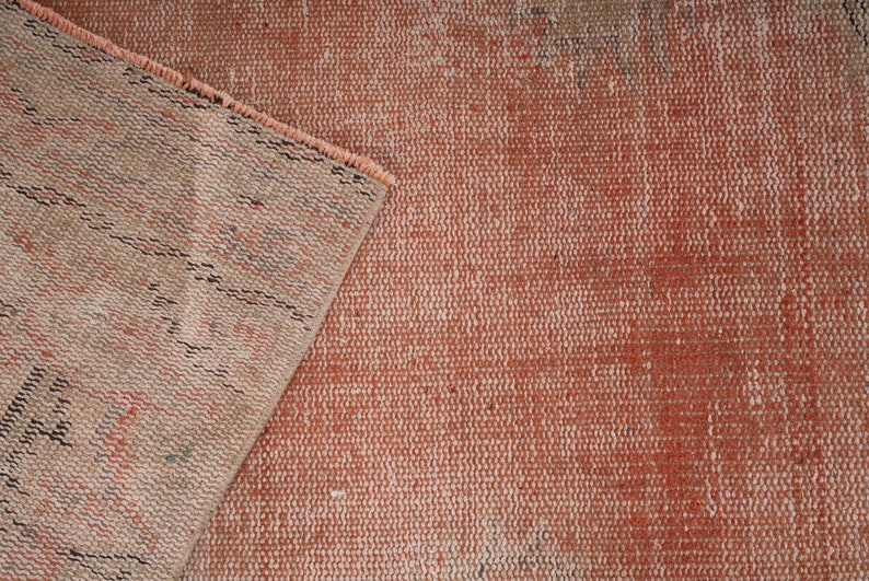 May include: Close-up of a woven rug with a faded red and white pattern. The rug has a textured surface and a frayed edge.