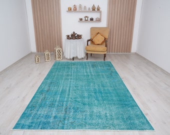May include: A teal blue vintage rug with a distressed look. The rug is laid out on a light wood floor in a room with white walls and a chair.