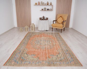 Pode incluir: Um tapete vintage tecido à mão com um fundo laranja desbotado e padrões florais intrincados em tons de azul, verde e bege. O tapete tem um visual desgastado e é perfeito para adicionar um toque de charme boémio a qualquer cômodo.