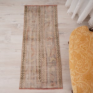 May include: A vintage-style runner rug with a faded, multi-colored pattern. The rug has a distressed look with a brown, beige, and pink color scheme. The rug is laid out on a light wood floor.