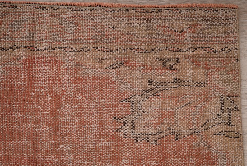 May include: Close-up of a vintage rug with a faded peach and beige color scheme. The rug has a woven pattern with a geometric design.