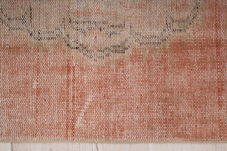 May include: Close-up of a woven rug with a textured surface. The rug has a light brown and orange color with a darker brown pattern.