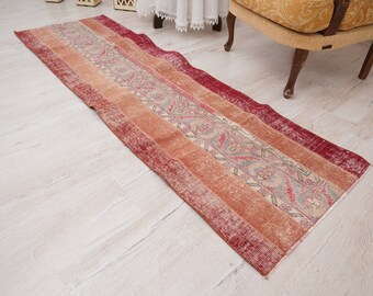 May include: A long, rectangular runner rug with a red, orange, and cream color scheme. The rug has a floral pattern with a faded, vintage look.