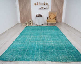 May include: A large, rectangular turquoise rug with a distressed, vintage appearance. The rug has a faded, mottled pattern and is placed on a light-colored wooden floor. The rug is a statement piece for a living room or bedroom.