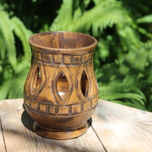 May include: A brown ceramic candle holder with a geometric design and cut-out details. The holder has a wide base and a narrow opening at the top.
