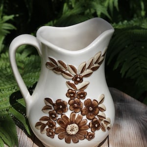 May include: A white ceramic jug with a brown floral design. The jug has a wide mouth and a handle.