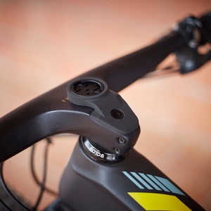 Può includere: Primo piano di un manubrio di bicicletta nero con uno stelo nero e un supporto per computer nero e grigio. Lo stelo ha una vite nera e il testo "ROTOR" è visibile sullo stelo.