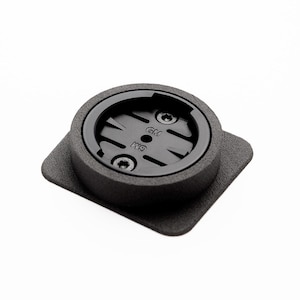 Könnte beinhalten: Schwarzer runder Fahrradhalter mit quadratischem Sockel. Der Halter hat eine strukturierte Oberfläche und eine kreisförmige Öffnung mit einer kleinen schwarzen Schraube in der Mitte. Der Text "GTL" und "K9" ist auf dem Halter sichtbar.