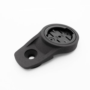 May include: A black bicycle computer mount with a textured surface. The mount has a circular top with a recessed area and a rectangular base with a hole. The mount is designed to hold a cycling computer.