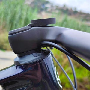 Op de afbeelding: Close-up van een zwart stuur van een fiets met een zwarte rubberen bevestiging aan de bovenkant. Het stuur is gemonteerd op een zwart en blauw fietsframe.