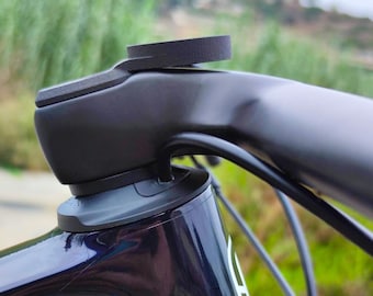 May include: Close-up of a black bicycle handlebar with a black rubber mount attached to the top. The handlebar is mounted to a black and blue bicycle frame.