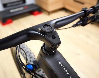 May include: A close-up shot of a black bicycle handlebar with integrated components. The handlebar has a built-in computer mount and a sleek design. The bike's frame is visible, with the text "F-PODIUM" printed on it. The tyres are grey and black.