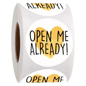 May include: Roll of round stickers with a yellow heart and the text "Open Me Already!" printed in black.