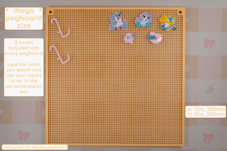 以下が含まれることがあります： 黄色いメガペグボード、幅305mm、高さ305mm、格子模様。ピンク色のフック2本と、カラフルな漫画のキャラクターの装飾がいくつか含まれています。ボードにはサイズとフックの色オプションが表示されています。