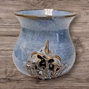 May include: A light blue ceramic vase with a textured glaze and a three-dimensional floral design in gold.