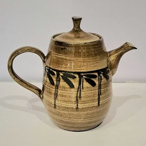 May include: A brown ceramic teapot with a black leaf design. The teapot has a lid and a handle.