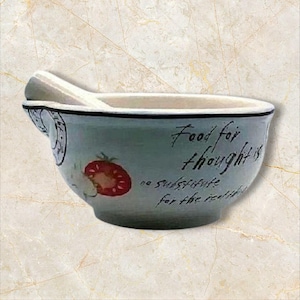 May include: A white ceramic mortar and pestle with a blue rim and a strawberry design. The mortar has the text "Food for thought is no substitute for the real thing" printed on it.