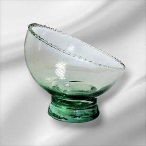 May include: A clear glass bowl with a scalloped rim and a green glass base. The bowl is angled and sits on a white surface.