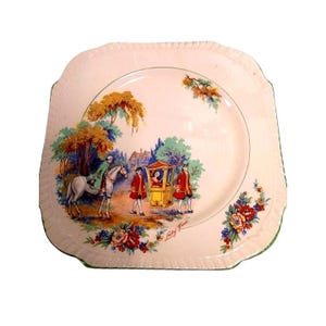 May include: Square ceramic plate with a decorative scene. The plate features a pastoral scene with figures in period clothing, a horse, and a carriage. Floral and foliage accents frame the design, with a green border. The words "Lady June" are written on the plate.