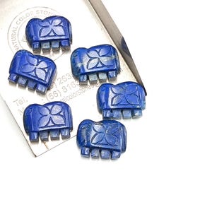 May include: Six carved lapis lazuli elephant figurines. Each figurine is a deep blue color with a carved floral design on its back. The elephants are displayed on a silver tray against a white background. The tray has text and a logo.