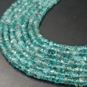 May include: Close-up of a strand of turquoise-colored gemstone beads. The beads are small, square-cut, and strung together, creating a textured, layered effect. The color is a vibrant, translucent teal, with hints of white and gray.