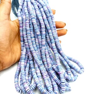 May include: A bundle of light blue and lavender disc-shaped beads. The beads are held together by a dark blue string. The beads are small and uniform in size, with a slightly iridescent finish. The beads are likely for jewelry making.
